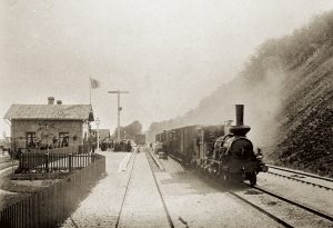 Båstad järnvägsstation 1885. Stationsbyggnaden var klar 1884, i god tid före invigningen den 9 maj 1885. OBS! Den nästan trädlösa åssluttningen.